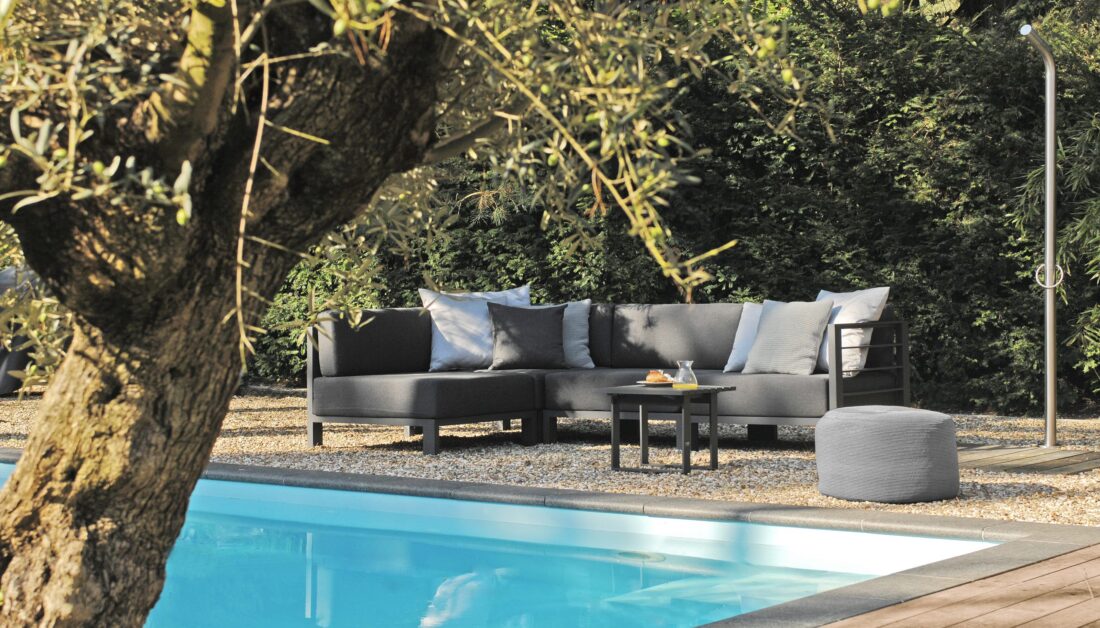 Mediterrane Terrassen Idee mit gemütlicher Sitzecke auf Kies vor dem großen Pool - grauer Outdoor Sitzsack & schwarzer Ablagetisch für den Garten
