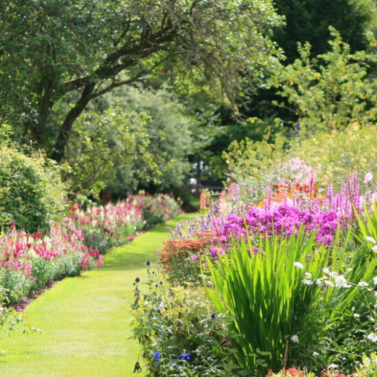 Gartenidee - Farbenfrohe Parkanlage mit blühenden Blumenbeeten und schattenspendenden Laubbäumen