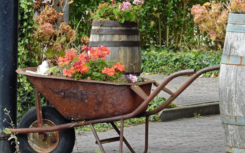Gartendekoration zum selber machen – Blumen in einer Schubkarre und Fässern im Hof