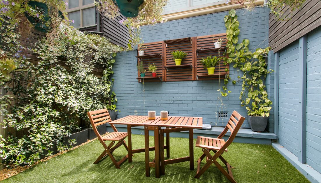 Idee für einen Garten im Innenhof mit Terrasse - Innenliegender Garten an Hauswand mit Stühlen und Tisch aus Holz - Gartenregal mit Pflanzen in Pflanzkübeln