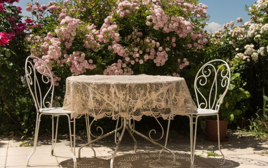 Idee für einen Sitzbereich im Garten – Gartentisch und Stühle aus Metall vor schönen Sträuchern mit Blumen
