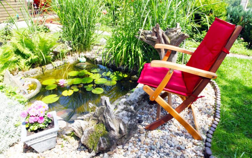 Idee für einen kleinen Teich mit Sitzbereich – gemütlicher Klappstuhl & Blumentopf mit Pflanze – Wasserpflanzen & Sträucher um den Teich