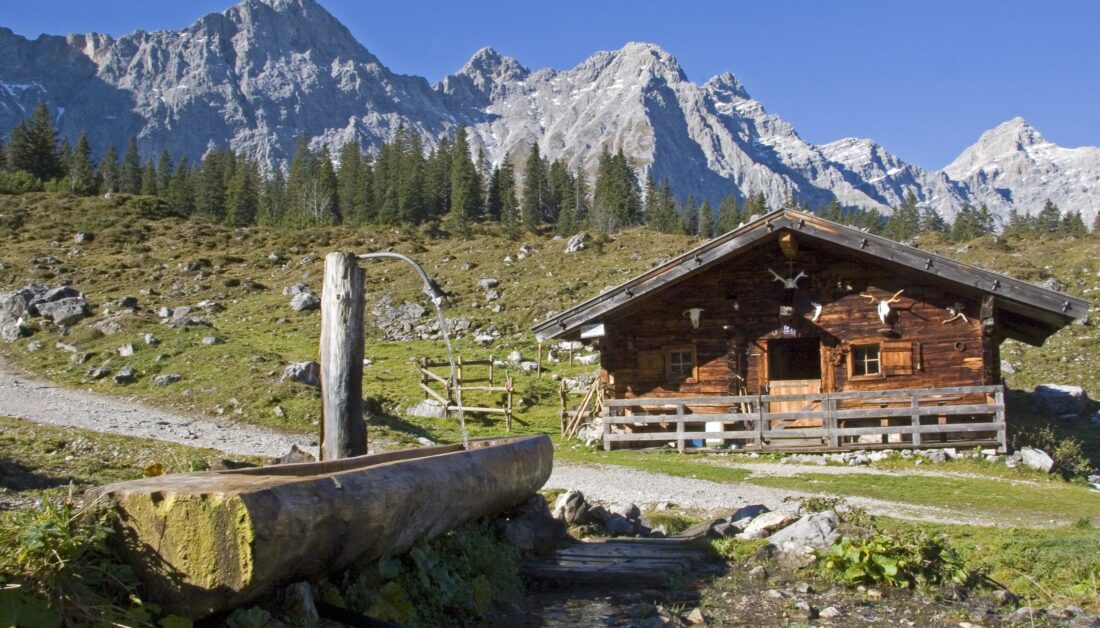 Wanderweg mit Berghütte mit Bachlauf und Holzbrunnen
