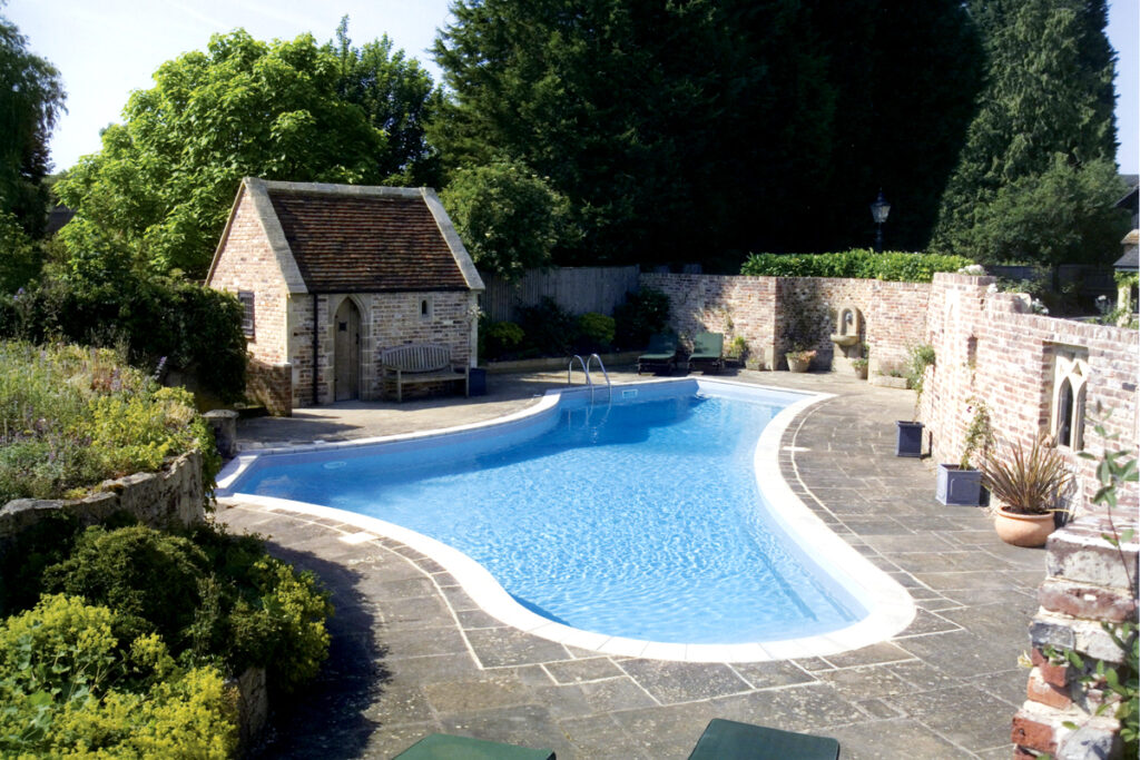 Steinterrasse mit Pool, Gartenhaus und Steinmauer als Sichtschutz