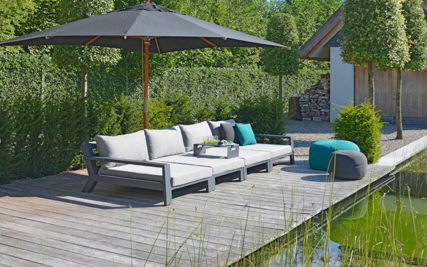 Idee für die Terrassengestaltung mit einem großen Gartensofa & Terrassen Sonnenschutz am Gartenteich – gemütliche Outdoor Sitzsäcke – kleine Bäume & Sträucher