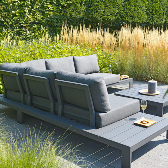 Idee mit moderner Loungegruppe auf einer Terrasse  umgeben von Ziergräsern & Heckensträuchern - Beispiel für die Terrassengestaltung mit Sofa & Tisch