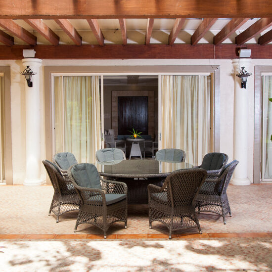 Idee für eine Terrasse im mediterranen Stil - Beispiel mit großen runden Tisch & Rattanstühlen unter einer Pergola aus Holz mit Steinsäulen - Außenwandleuchten & Pflanzen in Pflanzgefäßen