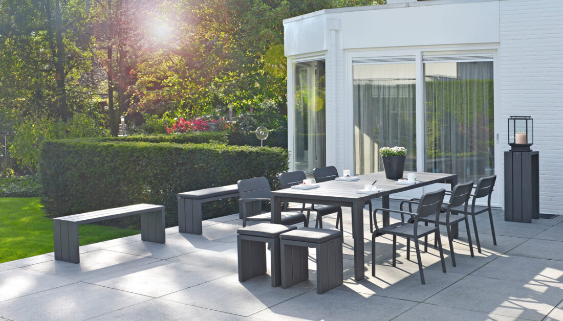 Moderne Terrassengestaltung mit Sitzgruppe - Beispiel mit schwarzen Tisch & schwarzen Stapelstühlen - schwarze Bänke & passend dazu ein Beistelltisch mit moderner Gartenlaterne - Hecken & Sträucher