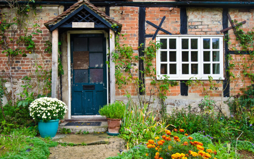 Landhausgarten Hauseingang Idee mit kleinen Vordach – Gestaltungsbeispiel mit Pflanzgefäßen  Kletterpflanzen an der Hauswand & Blumenbeeten