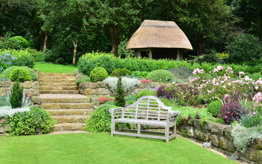 Großer Landhausgarten mit bepflanzten Stufenbeeten & Gartenbank als Gartenidee – Rustikales Gartenhaus umgeben von Bäumen & Sträuchern