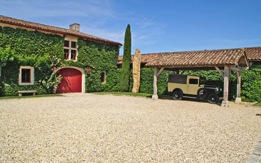 Mediterranes Landhaus mit rustikalen Carport als Vorgartenidee – Beispiel mit bepflanzter Hauswand mit Steinbank – Kiesfläche vor dem Haus