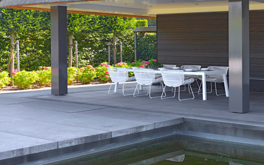 Überdachte Terrasse am Gartenteich Gestaltungsidee – Beispiel mit weiße Terrassenmöbeln – Gartenpflanzen auf einem Beet