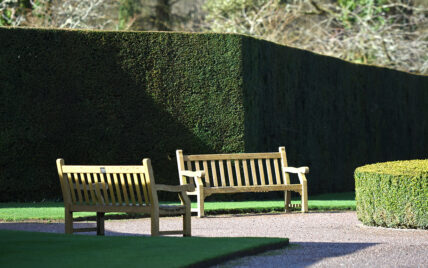 Idee für einen Sitzbereich im Garten oder Park – Beispiel mit zwei Holzbänken & hoher ...