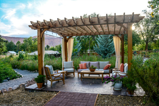 Terrassen Idee mit freistehender Terrassenüberdachung – Beispiel mit Gartensofa & Sesseln unter dem Gartenpavillon – Beistelltisch aus Holz – Pflanzgefäße mit Gartenpflanzen