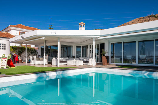 Gartenidee – Überdachte Terrasse am modernen Wohnhaus mit Sitzgruppe & Loungegruppe – Pool-Landschaft im Garten – Sichtschutz