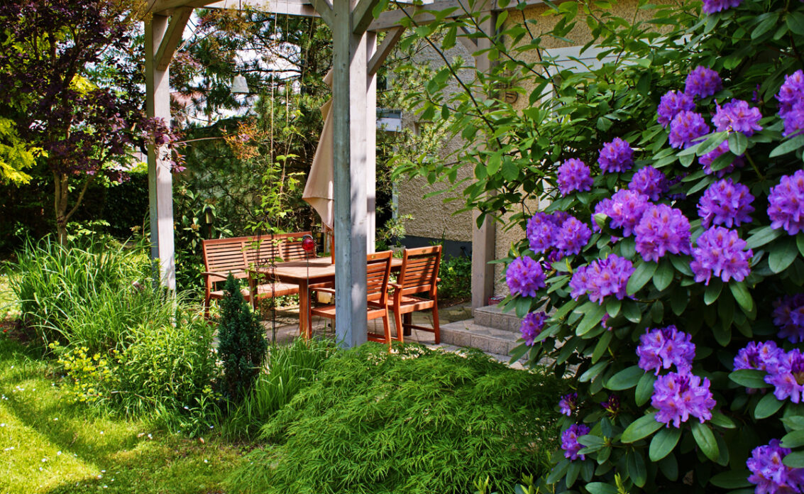 Idee für eine kleine Außenterrassse mit Sitzgruppe aus Holz – Blühender Rhododendron ...