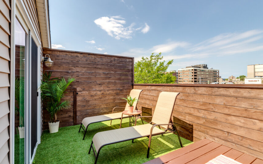 Balkon Idee mit Sichtschutz aus Holz & zwei Sonnenliegen – Metallbeistelltisch mit Pflanze – Außenwandleuchte – Balkonboden mit Kunstrasen