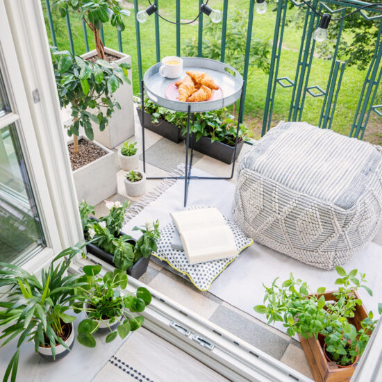 Beispiel für einen kleinen Balkon - Gestaltungsidee mit Sitzkissen  Metalltisch & vielen Pflanzen in Blumentöpfen - kleiner Teppich & Lichterkette als Beleuchtung & Dekoration