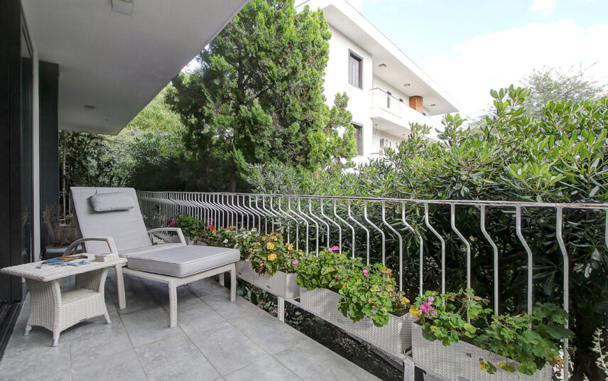 Moderne Idee für einen großen Balkon am Haus – Beispiel mit Rattansonnenliege & Rattantisch – Gemütliche Outdoor Polsterauflage – Bepflanzte Blumenkästen am Balkongeländer