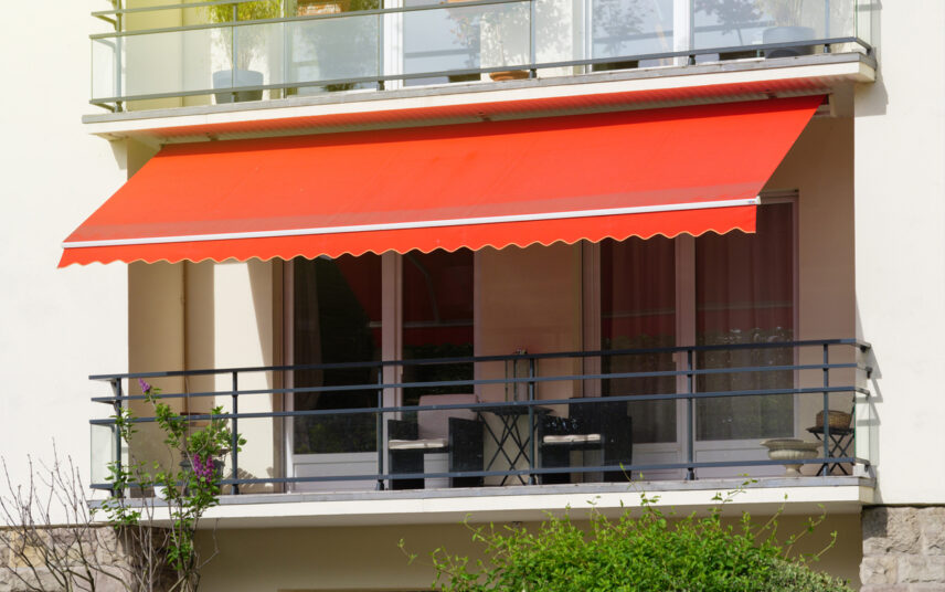Gestaltungsidee für einen schmalen Balkon – Beispiel mit roter Balkonmarkise als Sonnenschutz – Sitzbereich mit zwei Polyrattansessel  Metallbeistelltisch & Laterne als Dekoration