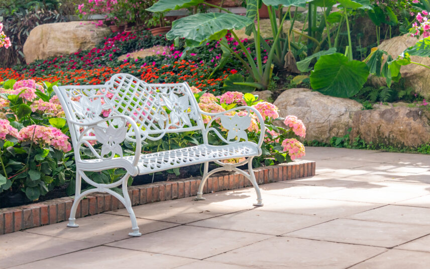 Gartengestaltung mit weißer rustikalen Gartenbank auf dem Gartenweg – Farbenfrohes Beet mit rosa Hortensien – Hang mit Sommerblumen & tropischer Pflanze