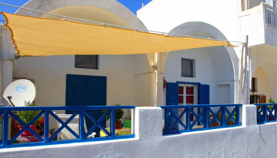 Griechischer Balkon mit Sonnensegel als Sonnenschutz - Idee für die mediterrane Balkongestaltung mit blauem Geländer & weißer Hauswand - Sitzgruppe & Pflanzgefäße
