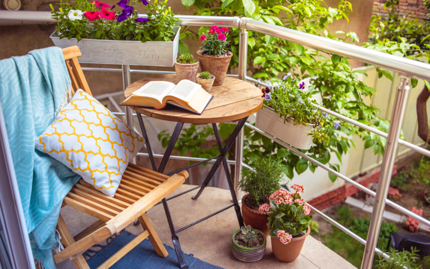 Idee für einen kleinen Balkon – Beispiel mit Klapptisch & Klappstuhl mit Kissen & Decke – viele kleine Pflanzgefäße mit Blumen – Blumenkasten am Balkongeländer
