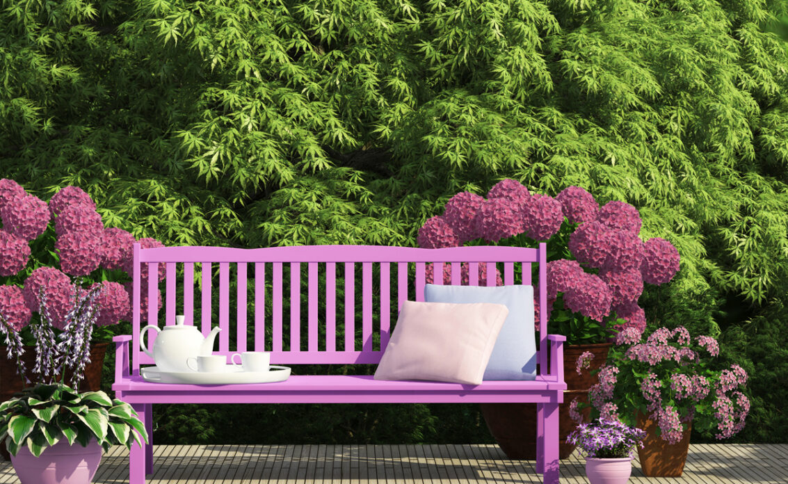Beispiel für den Garten – Idee für eine Sitzecke mit lila Bank  & Kissen umgeben von G...