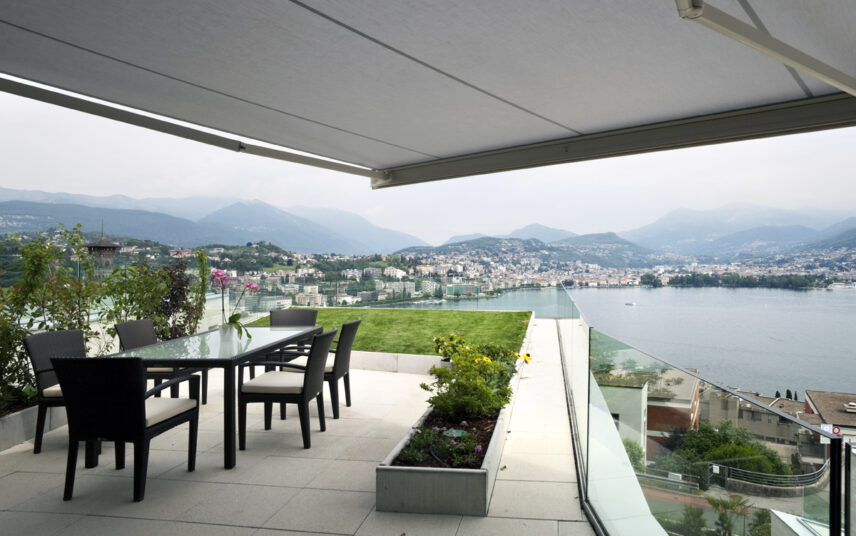 Balkon Idee – Großer Luxus Balkon mit schwarzer Sitzgruppe aus Polyrattan & Balkonmarkise als Sonnenschutz & Überdachung – Pflanzen & Rasenfläche