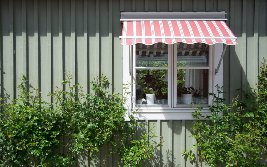 Hauswand Idee im Landhausstil – Rot gestreifte Gelenkarm-Markise außen am Fenster als Sonnenschutz – Gartenpflanzen an der Hauswand
