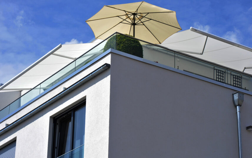 Sonnenschutz Idee für den Balkon oder die Dachterrasse – Beiger Sonnenschirm & weiße Sonnenschutzmarkisen an der Hauswand – Großer Buchsbaum als Balkon Dekoration