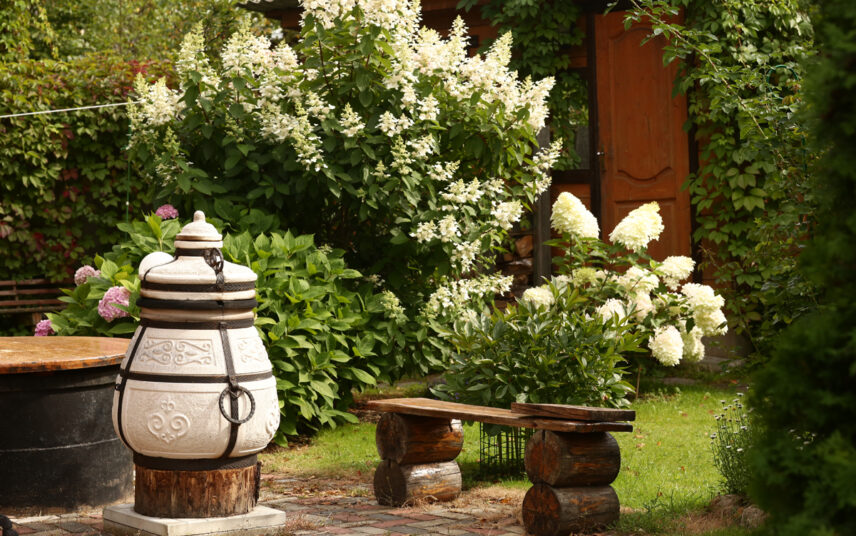 Gestaltungsidee für einen gemütlichen Garten mit Essplatz – Kleine Holzbank & Gartenofen – Weiße Hortensien (Hydrangea) & weitere Gartenpflanzen
