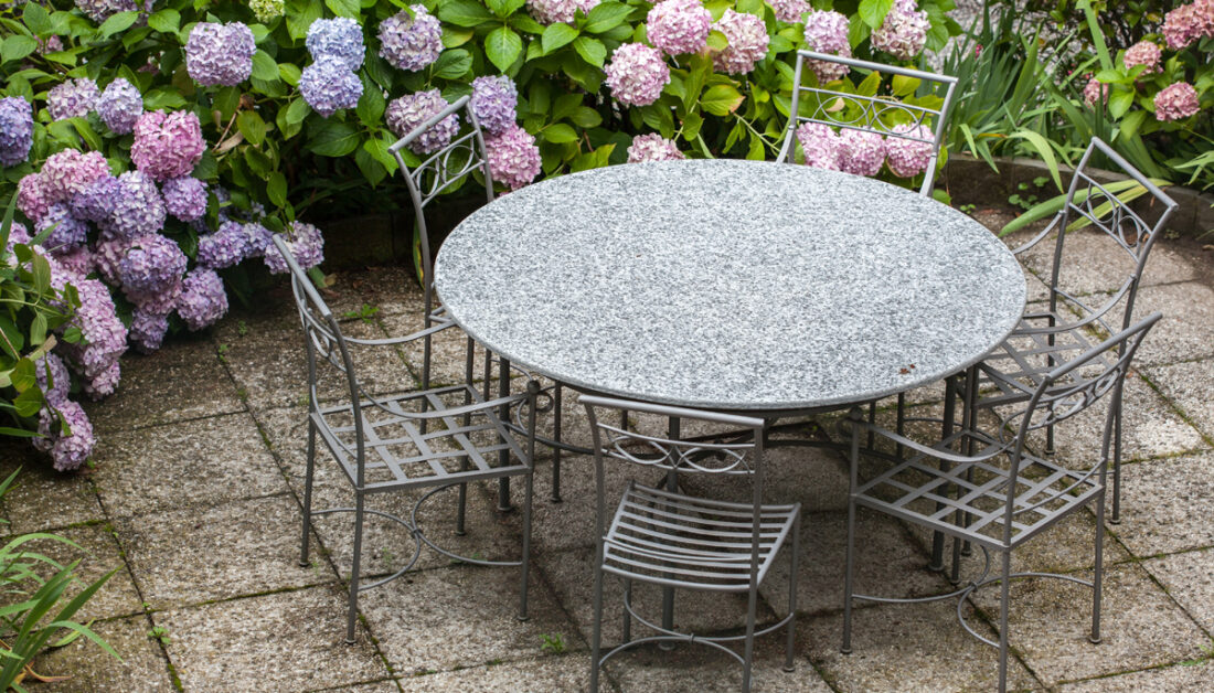 Gartenidee - Sitzgruppe aus Metall auf der Terrasse umgeben von lila & rosa Hortensien - Runder Tisch & Stühle aus Schmiedeeisen