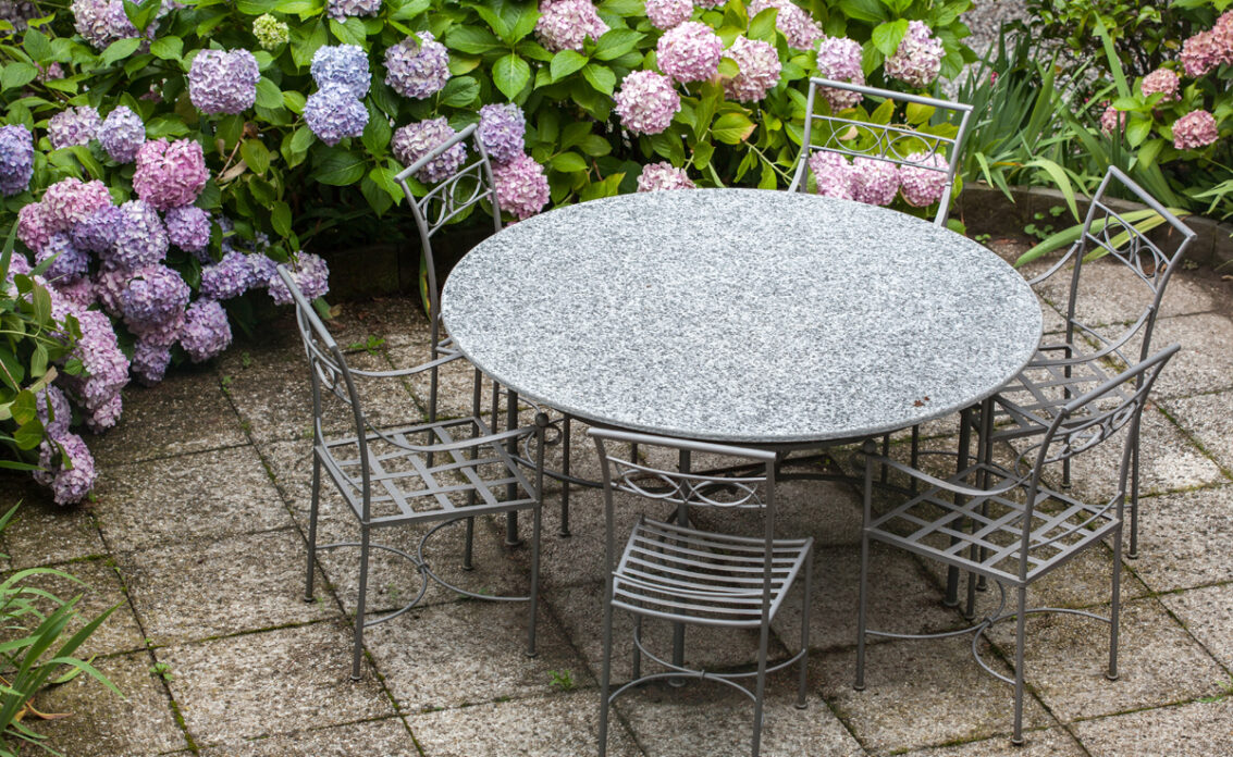 Gartenidee – Sitzgruppe aus Metall auf der Terrasse umgeben von lila & rosa Hortensien �...
