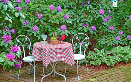 Garten Gestaltungsidee – Sitzgruppe aus Metall vor lila Rhododendron – Karierte Tischd...