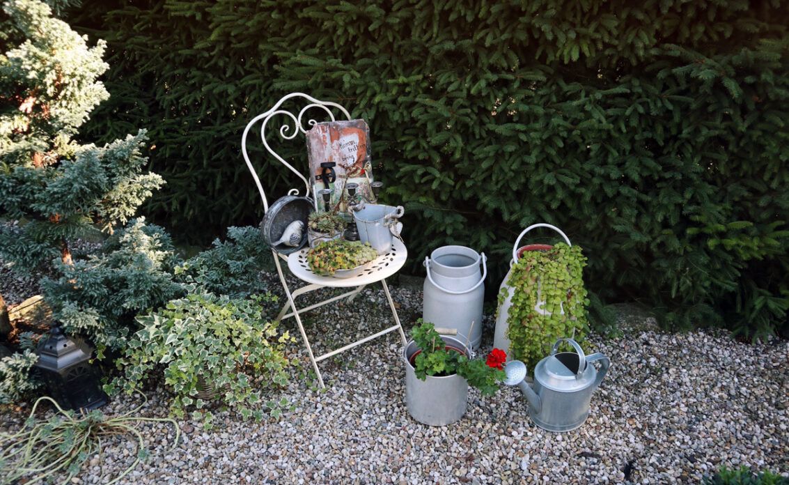 Gestaltungsidee für einen kleinen Steingarten an der Hecke  dekoriert mit Stuhl  Pflanzge...