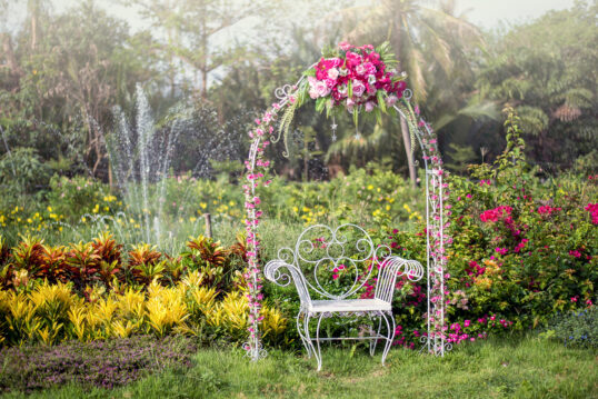 Romantische Gartenidee – Weißer Metallstuhl unter einem dekorierten Rosenboge...