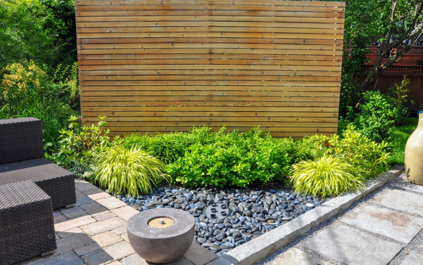 Gartengestaltung mit einer Sichtschutzwand aus Holz – kleiner Steingarten mit Pflanzen – runder Brunnen & Terrassenmöbel aus Polyrattan