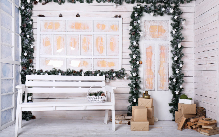 Hauseingang Idee – Dekorative Veranda mit Weihnachtdekoration – Weiße Gartenbank mit Korb – Weihnachtsgirlanden mit Dekokugeln an der Hauswand