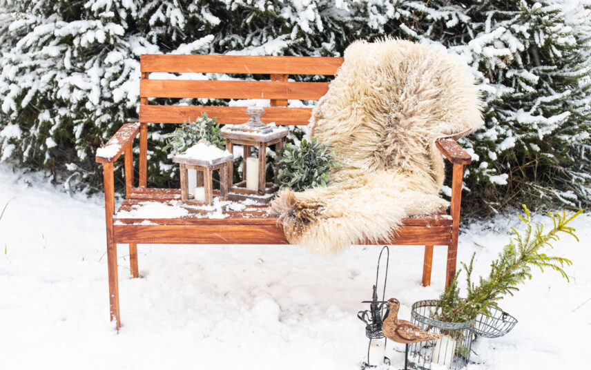 Idee für die winterliche Sitzplatz Gestaltung im Garten – Dekorierte Gartenbank aus Holz mit Fellteppich & Holzlaternen – Dekofiguren im Schnee