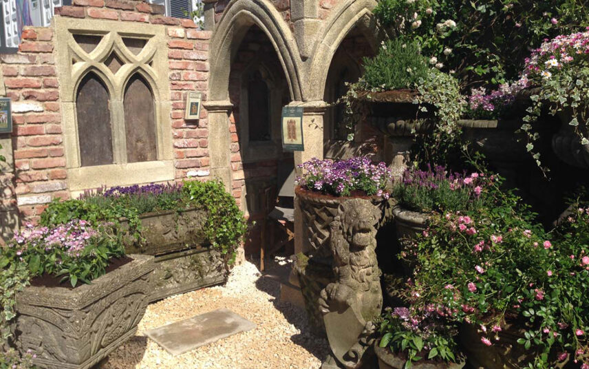 Beispiel für die Gartengestaltung – Gartenruine im gotischen Stil mit integrierten Pflanzkübeln & dekorativen Figuren – Bunte Blumen & Sträucher