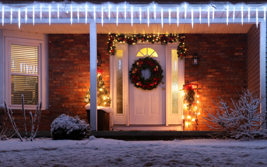 Idee für ein Wohnhaus mit Weihnachtsdeko außen – Beispiel mit Weihnachtskranz & Weihnachtsgirlande an der Haustür – Geschmückter Weihnachtsbaum im Pflanzgefäß