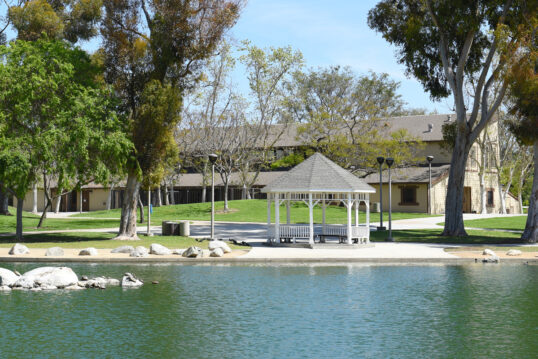 Idee für die moderne Parkgestaltung – Weißer Pavillon aus Holz neben einem großen Schwimmteich – Dekorative Steine im Natur Pool & am Uferrand – Wegbeleuchtung mit Mastleuchten