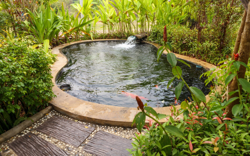 Moderne Gestaltung eines Schwimmteichs im immergrünen Garten – Beispiel mit kleinen Wasserfall & Wegplatten zum Gartenteich