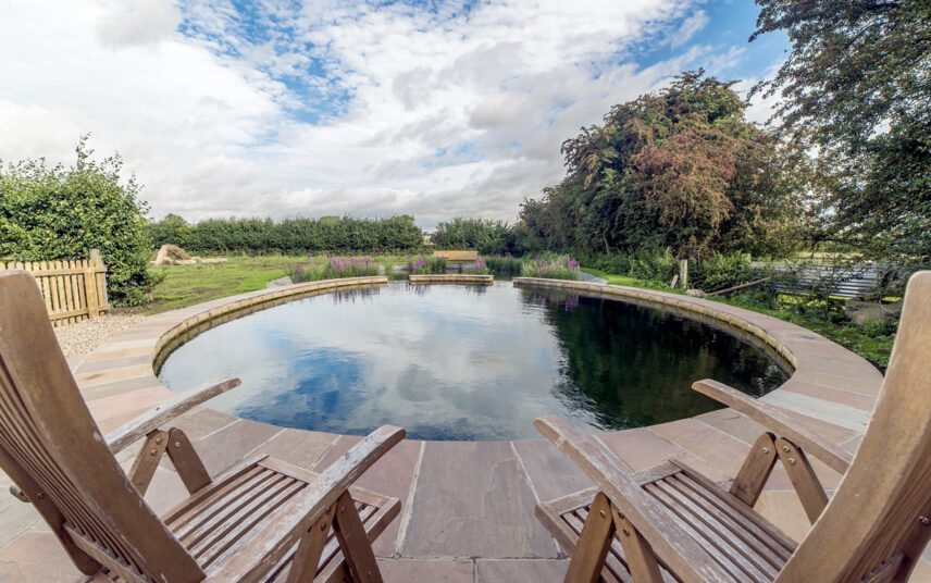 Moderner Schwimmteich mit angrenzender Terrasse – Beispiel mit Klappstühlen zum Entspannen nach dem Schwimmen