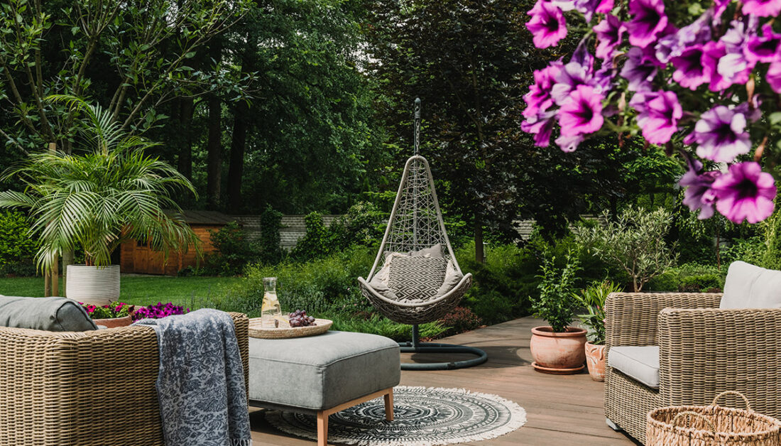 Boho-Stil Terrassengestaltung - Hängesessel  Hocker & Rattan-Sessel in einer Sitzgruppe - Verschiedene Pflanzen in Pflanzgefäßen als Dekoration