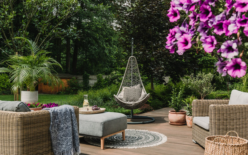 Romantische Gartenidee – Weißer Metallstuhl unter einem dekorierten Rosenbogen mit Strauß – Blumengarten mit rosa Rhododendren – Fontäne im Teich