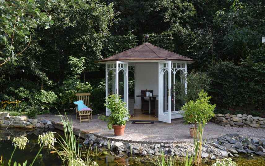 Terrasse am Gartenteich – Idee mit einem weißen Gartenpavillon & Sitzgruppe – Liegestuhl aus Teakholz & zwei Pflanzgefäße mit Bäumen
