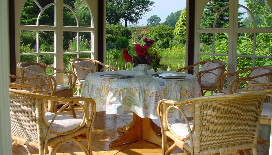 Terrassen Idee - Ausstattung eines Gartenpavillons mit Sitzgruppe aus Rattan - Tischdecke auf einem runden Tisch & Pflanzgefäß mit Blumen