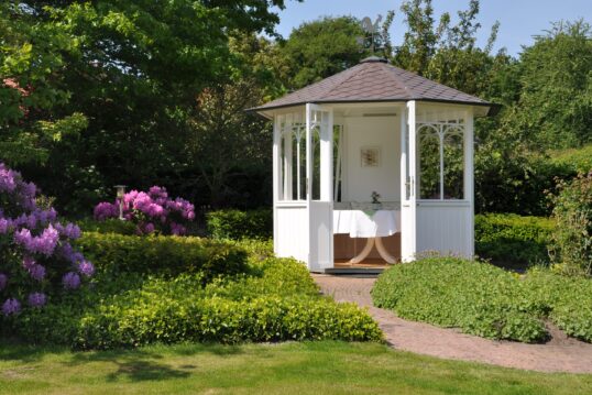 Exklusive Gartengestaltung mit Gartenpavillon – Weißes Pavillon auf der Wiese gepaart mit Sitzgruppe aus Holz